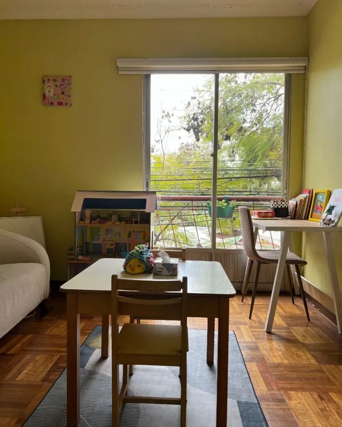 Box infantil con mesa de trabajo y casa de muñecas junto a la ventana